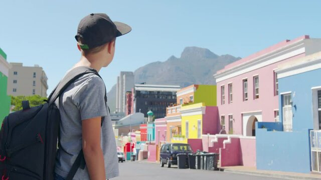 Boy tourist in Cape town Bo-Kaap Malay area, perspective of cobble stone street, colored terrace houses, laundry on line side of house.