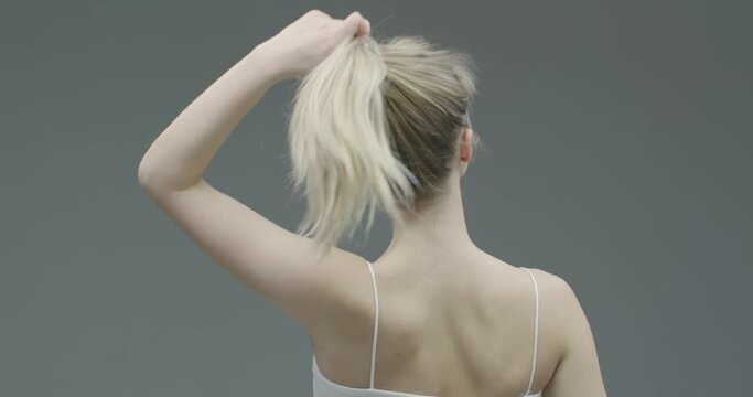 Pretty young blond girl take off scrunchie from hair satisfied with dyed hairs condition, morning routine, back view