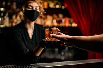 man's hand takes glass with cocktail from the hands of woman bartender