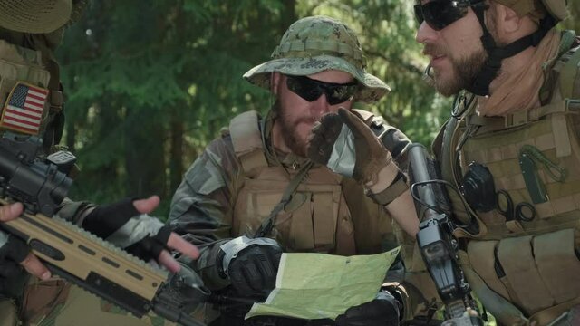 Handheld medium closeup of squad of professional disguised scouts with sniper rifles looking at map of area discussing plans during military operation