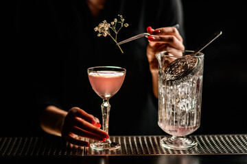 close-up of glass with pink alcoholic drink which woman decorates with sprig of white flower