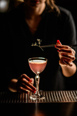 close-up of sprig of flower with which woman decorates glass with cocktail