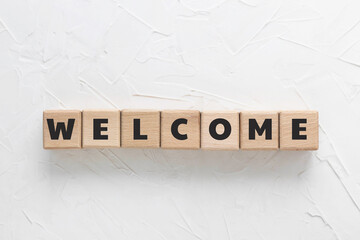 Text WELCOME made of wood cubes on white textured putty background. Square wood blocks. Top view, flat lay.