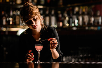 view of woman bartender that neatly decorates glass of cocktail with flower sprig