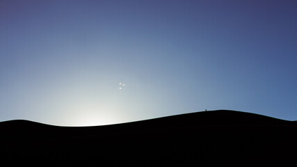 Black and blue wide shot of man standing on top of sandy dunes at sunset in great sand dunes national park in america