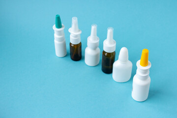 Bottles of nasal spray standing in line on blue background, medicine flat lay, treatment for colds, medical banner