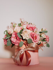 Bouquet with pink anemones and roses and eucalyptus branches in round pink box. Satin ribbon on the box. Present, spring time, happy women's day. On white background.