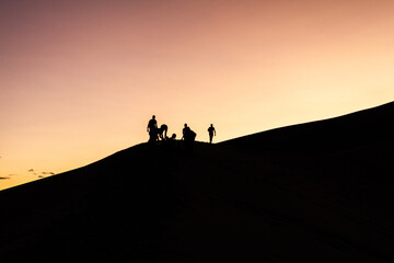 Fototapeta na wymiar Silhouette of group of people standing on top of sandy dune at colorful orange sunset in america