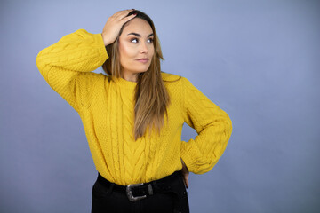 Young beautiful blonde woman with long hair wearing a yellow sweater putting one hand on her head...