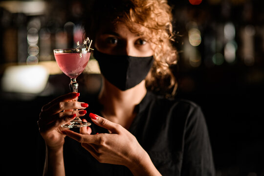 beautiful glass of cocktail decorated with flower in the hands of attractive woman in mask