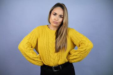 Young beautiful blonde woman with long hair wearing a yellow sweater skeptic and nervous,...