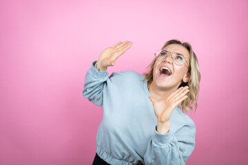 Young caucasian woman wearing sweatshirt over pink background scared with her arms up like something falling from above