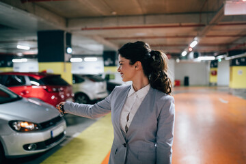 Elegant businesswoman locking her car with keys in underground parking.