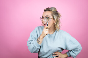 Young caucasian woman wearing sweatshirt over pink background surprised looking through a...