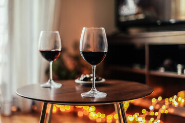 Romantic evening at home: two glasses of red wine, cosy light, tv on the background - obrazy, fototapety, plakaty
