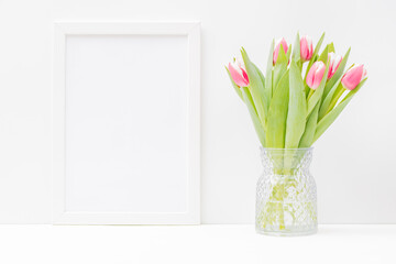 Home interior with decor elements. Mockup with a white frame and pink tulips in a vase on a light background