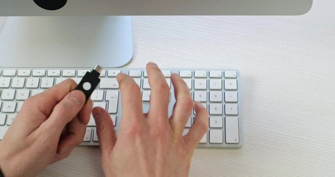 Close-up, a man in one hand holds an electronic password encoder, with the other hand he types a password on a computer keyboard. Modern password protection systems.