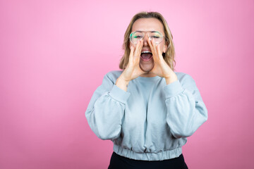 Young caucasian woman wearing sweatshirt over pink background shouting and screaming loud to side with hands on mouth