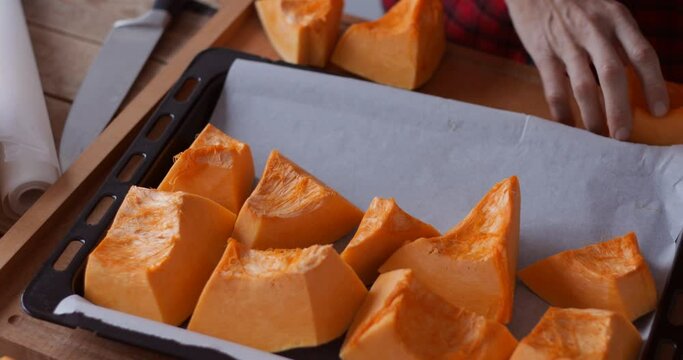 Sweet pumpkin roasting, arranging pieces onto baking tray, close-up
