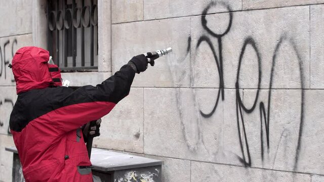 Worker cleans graffiti from a public building wall using pressure sand blaster.
