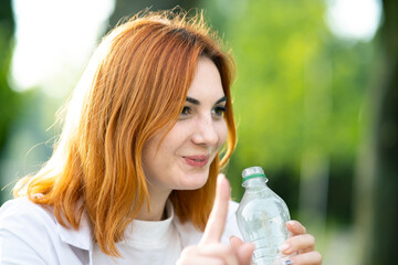 Young redhaired woman drinking water from a bottle on summer day.