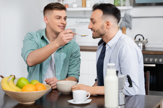 homosexual man feeding husband with corn flakes near cup and fruits