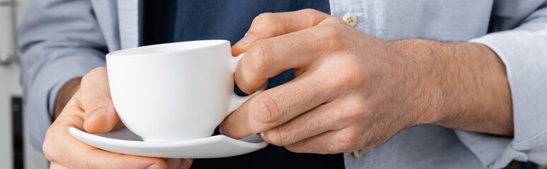 Fototapeta premium cropped view of man holding cup with coffee and saucer, banner