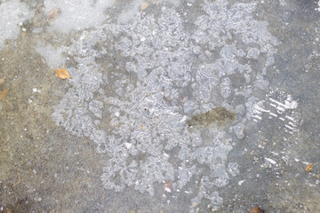 Abstract background. Blue ice with air bubbles and white snow, frozen lake or puddle water surface on cold winter day.