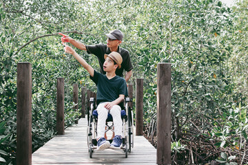 Asian special child on wheelchair and parent happy on mangrove forest background,Activity outdoor with family on travel holiday, Lifestyle in the education age of disabled children,Happy disabled kid.