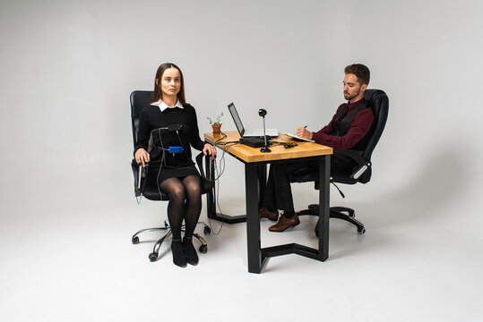 Concentrated, thoughtful woman is in a bright room, testing on a computer polygraph. Young man sitting at the table and looking at the polygraph screen and polygraph monitoring. The concept of truth, 