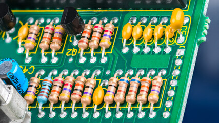 Closeup of printed circuit board with electronic components. Electrotechnics. Colorful resistors with standard color code, yellow or blue capacitors and black transistors on green PCB detail. E-waste.