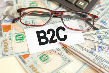 On the table are bills, a bundle of dollars and a sign on which it is written - B2C. Business and Finance concept.
