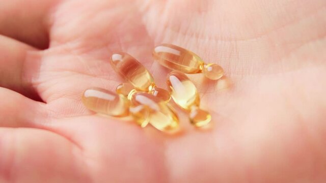 Close up of hand holding yellow transparent capsules pills organic vitamins fish oil from meds bottle. Diet nutrition and healthy concept. Vitamin D, E, A,  Omega 3.