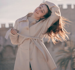 Stylish portrait of a beautiful young woman on the streets of Valencia in a brown jersey on a sunny day at sunset posing and smiling.