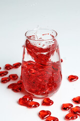 Valentine's Day. Small red glass hearts in a glass of water. A splash of liquid.