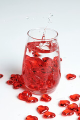 Valentine's Day. Small red glass hearts in a glass of water. A splash of liquid.