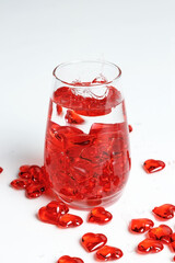 Valentine's Day. Small red glass hearts in a glass of water. A splash of liquid.