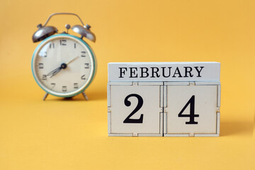 Calendar for February 24: cubes with the number 24 and the name of the month, alarm clock on a yellow background
