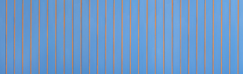 Blau gestrichene Panorama Holzwand mit aufgesetzten, vertikalen, orangen Holzleisten