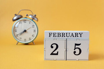 Calendar for February 25: cubes with the number 25 and the name of the month, alarm clock on a yellow background
