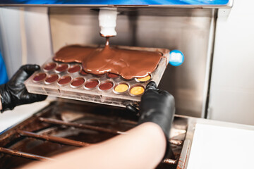 Professional confectioner pouring melted black chocolate into silicone mold.