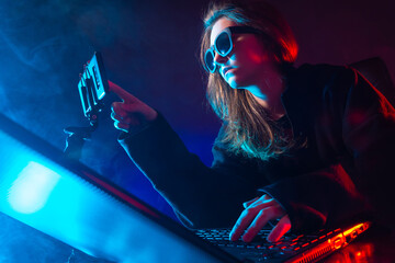 Geek woman next to a laptop. She uses a cell phone. Portrait of a geek woman in a dark room. Geek...