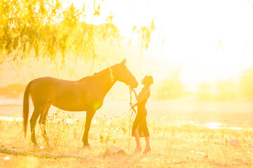 A girl stands in front of a horse, they are bathed in warm sunbeams at sunset