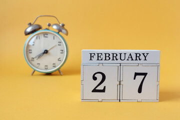 Calendar for February 27: cubes with the number 27 and the name of the month, alarm clock on a yellow background