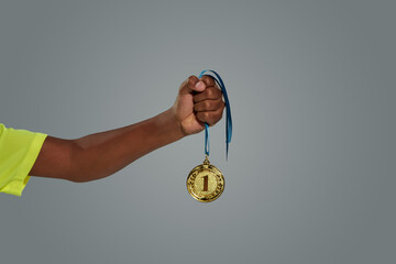 Plakat Award of victory. Teenage african boy holding gold medal against grey background