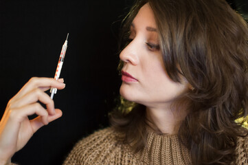 Obraz premium Vaccine concept. Female portrait of caucasian girl holding a syringe and looking at it on black background in studio.