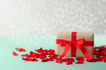 Gift box with a red bow ribbon and a red petals on a table for  Valentine's day.
