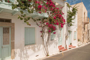 Fototapeta na wymiar Stone houses with white and terra painted walls, wooden shutters and grown with red flowers in Chora, Kythira, Greece