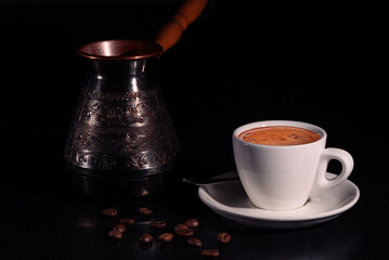 White cup of coffee, copper cezve and coffee beans on black wooden table. Low key. Copy space.