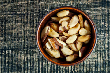Brazil nuts in a clay bowl on a wooden table. Nuts on a black shabby board. Copy space and free space for text near nuts.